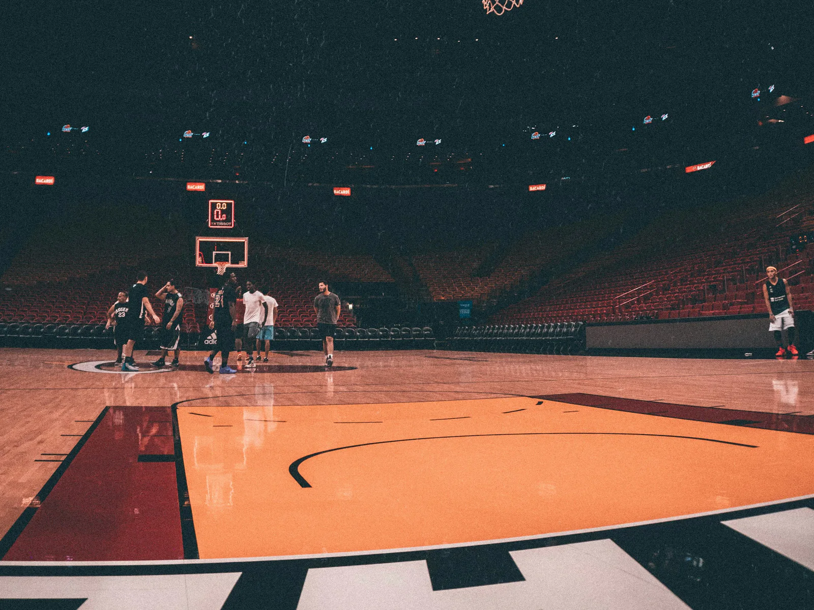 Basketball players practicing beneath arena lights on an orange court